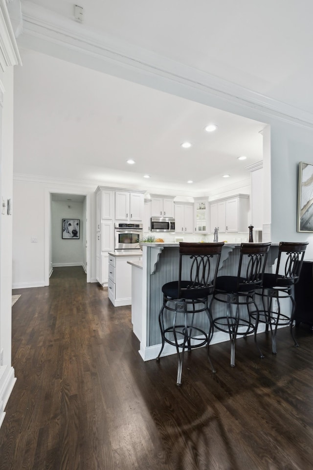 kitchen with dark wood-style flooring, a breakfast bar area, stainless steel appliances, white cabinetry, and a peninsula