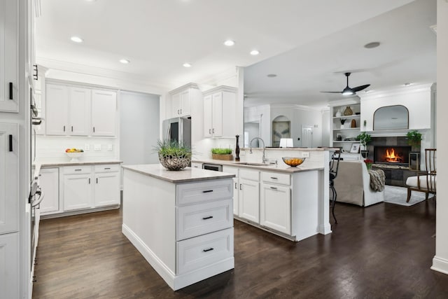 kitchen with a peninsula, a fireplace, a sink, white cabinetry, and open floor plan