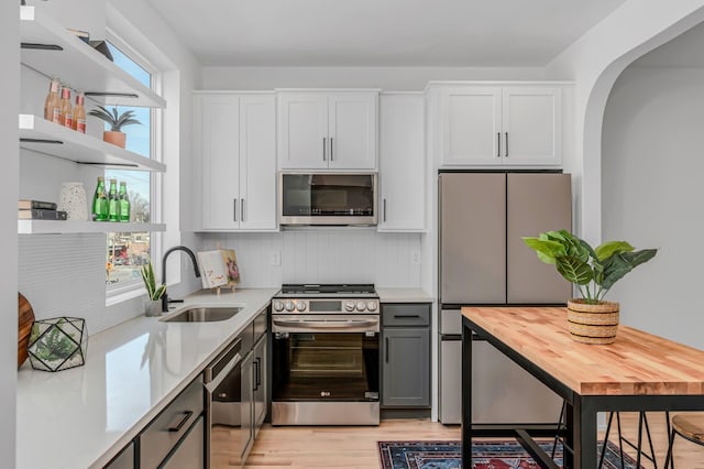 kitchen featuring stainless steel appliances, a sink, light countertops, decorative backsplash, and open shelves