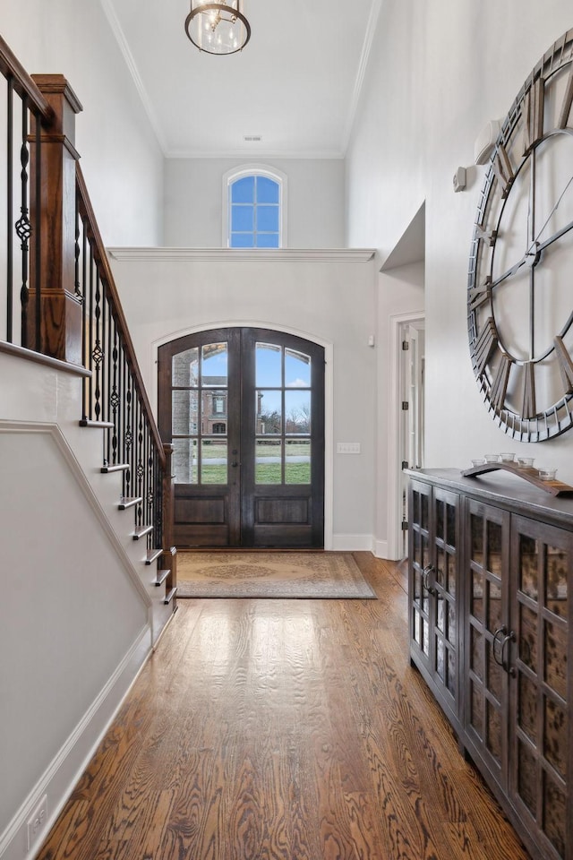 foyer entrance with french doors, crown molding, stairway, wood finished floors, and baseboards