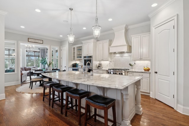 kitchen featuring dark wood-style flooring, tasteful backsplash, custom range hood, an island with sink, and a kitchen bar