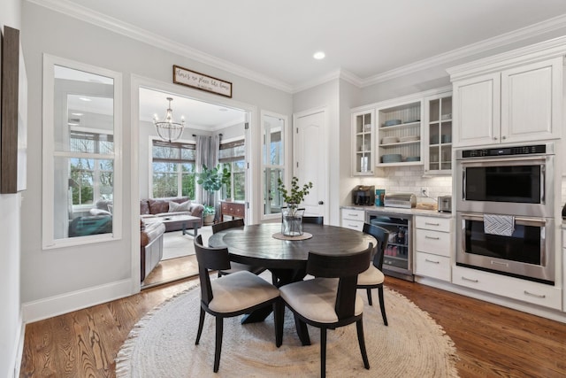 dining area with wine cooler, dark wood-style flooring, an inviting chandelier, ornamental molding, and baseboards