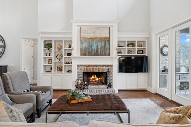 living room with a brick fireplace, a high ceiling, and wood finished floors