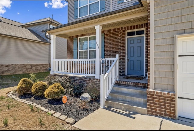 property entrance with a porch, brick siding, and a garage