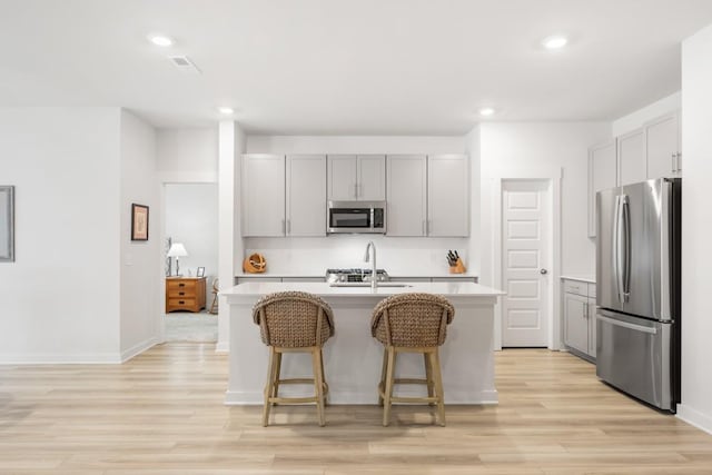 kitchen with gray cabinetry, a sink, light countertops, appliances with stainless steel finishes, and a center island with sink