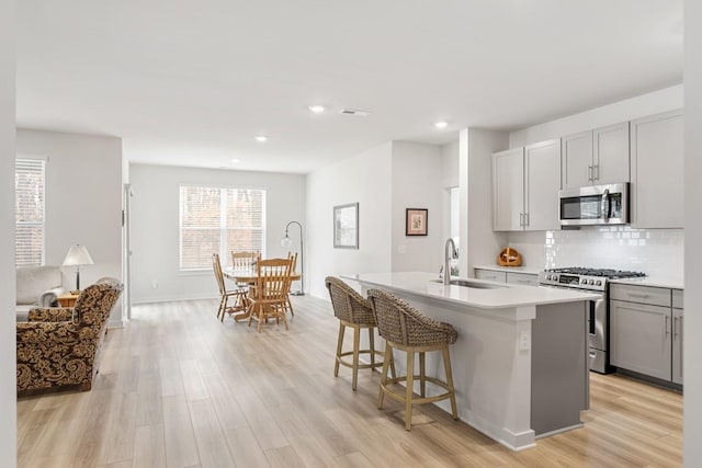 kitchen with a center island with sink, stainless steel appliances, tasteful backsplash, gray cabinetry, and a sink