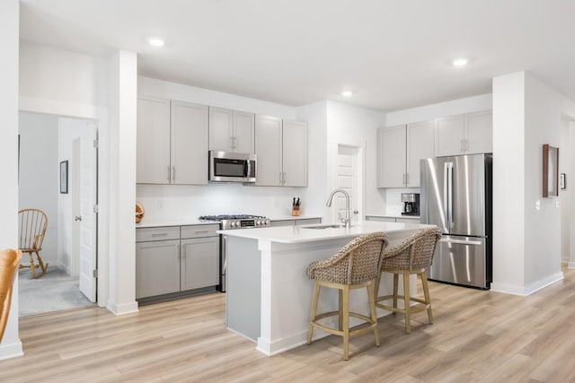 kitchen with gray cabinets, appliances with stainless steel finishes, a kitchen island with sink, a sink, and light wood-type flooring