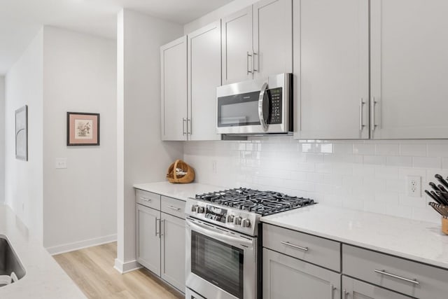 kitchen featuring stainless steel appliances, light wood-style floors, gray cabinets, light stone countertops, and tasteful backsplash