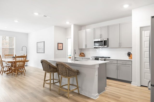 kitchen featuring stainless steel microwave, stove, gray cabinets, light wood-type flooring, and a sink