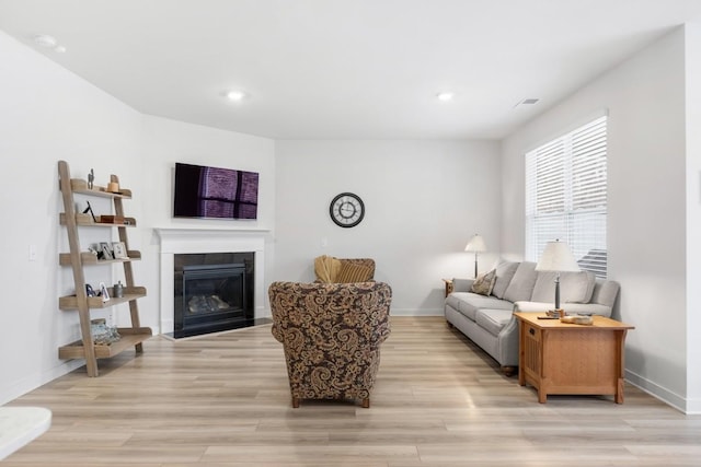 living room featuring a fireplace with flush hearth, light wood-style flooring, and baseboards