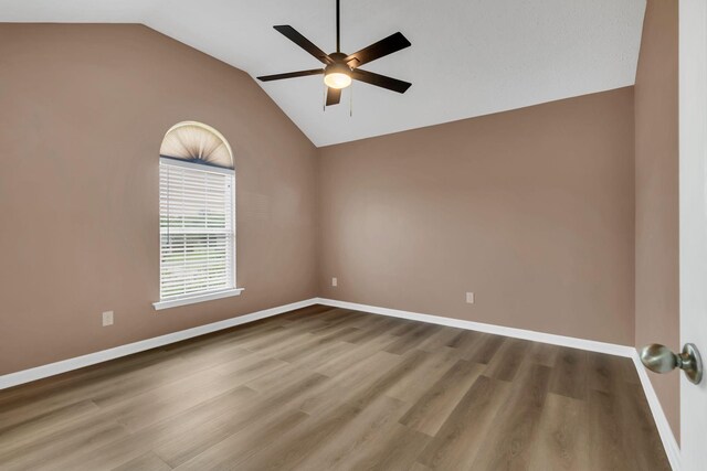 spare room with ceiling fan, vaulted ceiling, baseboards, and wood finished floors