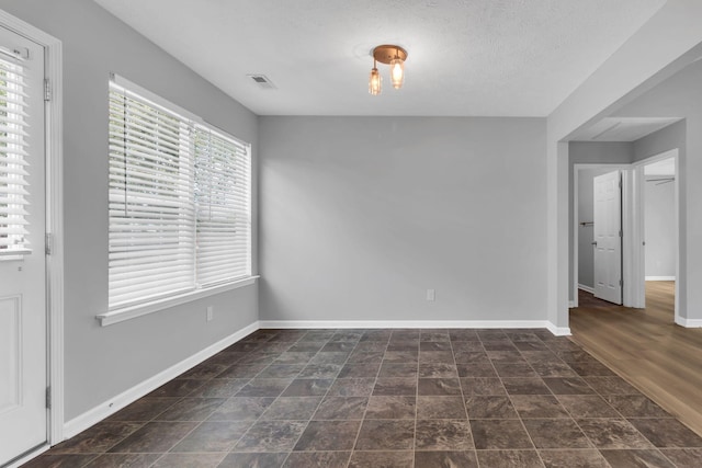 spare room featuring stone finish floor, baseboards, visible vents, and a textured ceiling