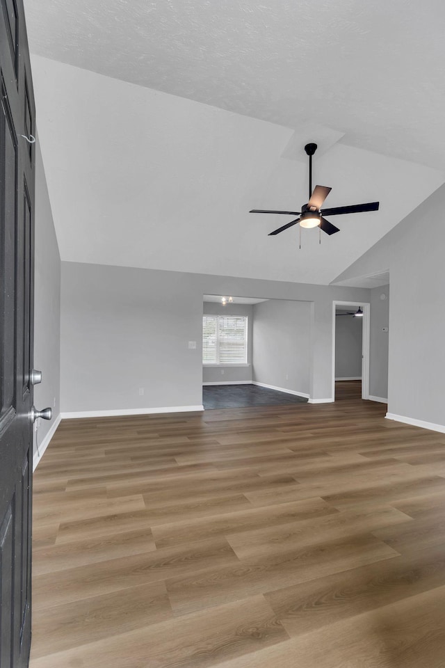 unfurnished living room with vaulted ceiling, ceiling fan, wood finished floors, and baseboards