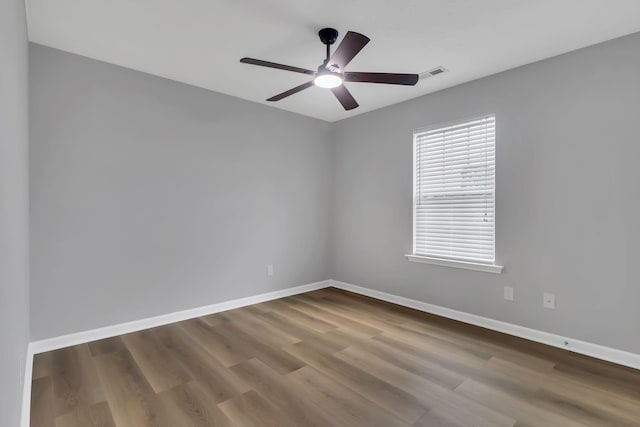 spare room featuring a ceiling fan, visible vents, baseboards, and wood finished floors