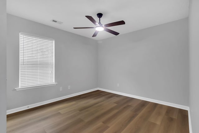 empty room featuring dark wood-style floors, visible vents, and baseboards