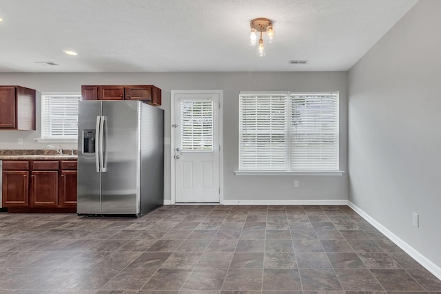 kitchen with a sink, visible vents, baseboards, light countertops, and stainless steel fridge with ice dispenser