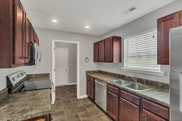 kitchen with appliances with stainless steel finishes, dark countertops, a sink, and visible vents