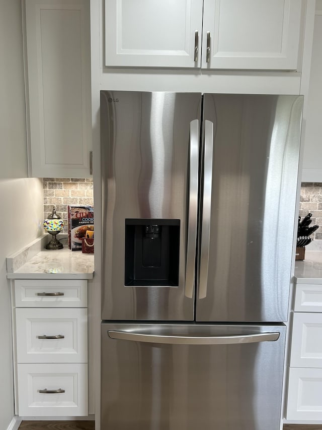 room details featuring light stone counters, backsplash, white cabinetry, and stainless steel refrigerator with ice dispenser