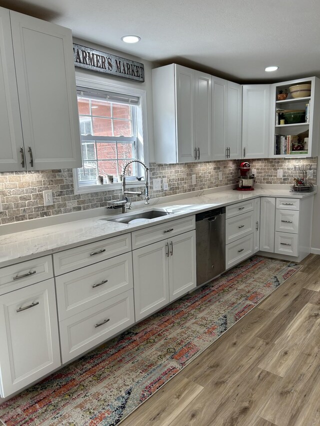 kitchen with tasteful backsplash, white cabinets, dishwasher, light wood-style floors, and a sink