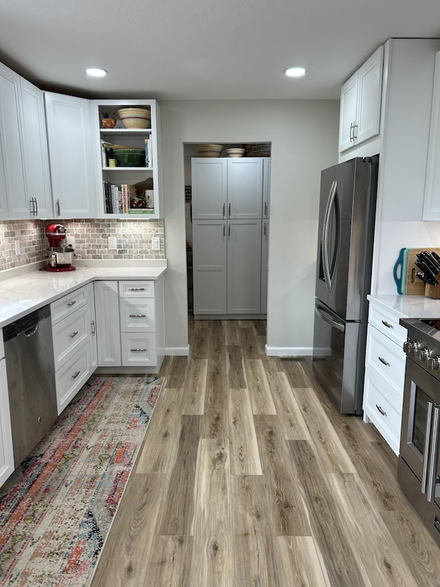 kitchen featuring light wood-style flooring, stainless steel appliances, white cabinets, light countertops, and backsplash