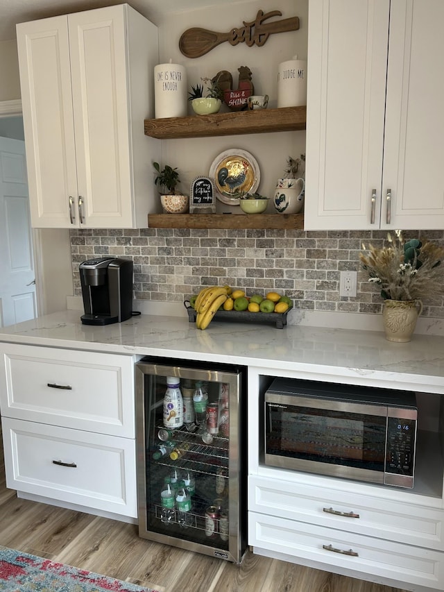 bar with beverage cooler, wood finished floors, a dry bar, tasteful backsplash, and stainless steel microwave