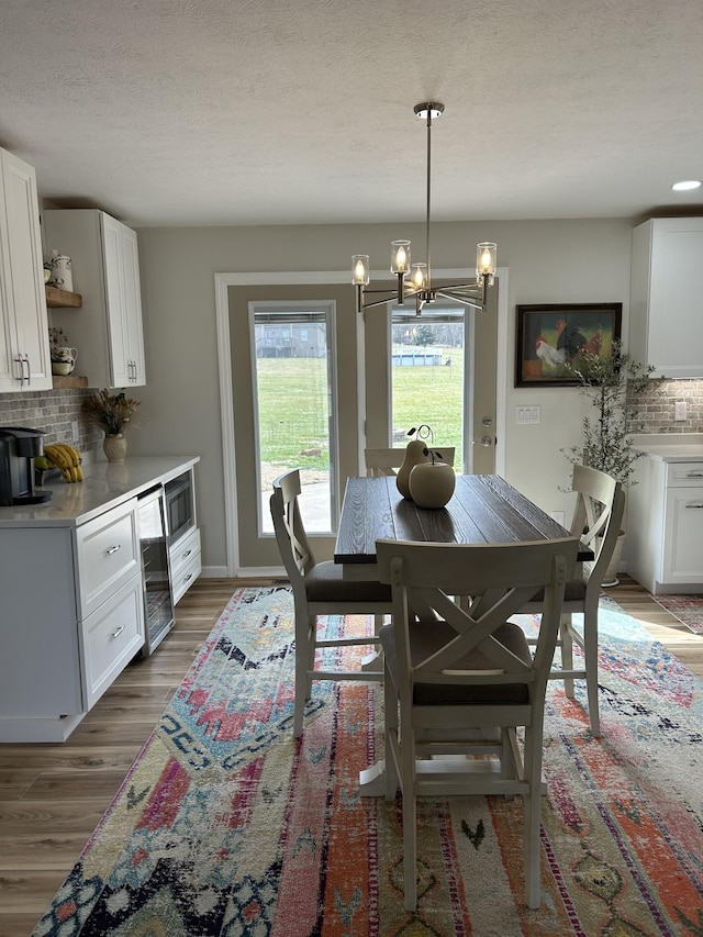 dining space with a notable chandelier, light wood-style flooring, a textured ceiling, beverage cooler, and baseboards