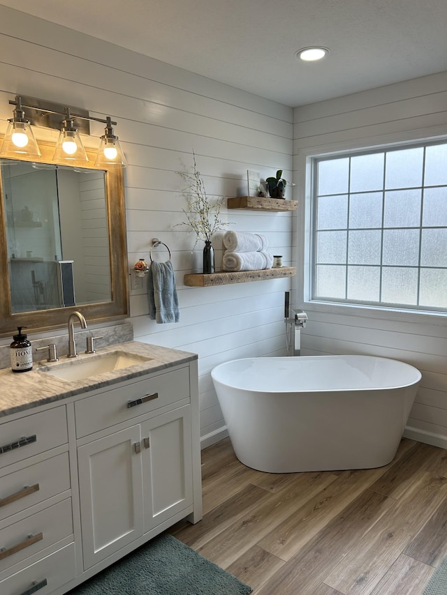 bathroom with a freestanding tub, wood finished floors, vanity, and recessed lighting