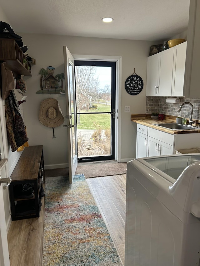 washroom featuring washer / dryer, cabinet space, baseboards, light wood-type flooring, and a sink