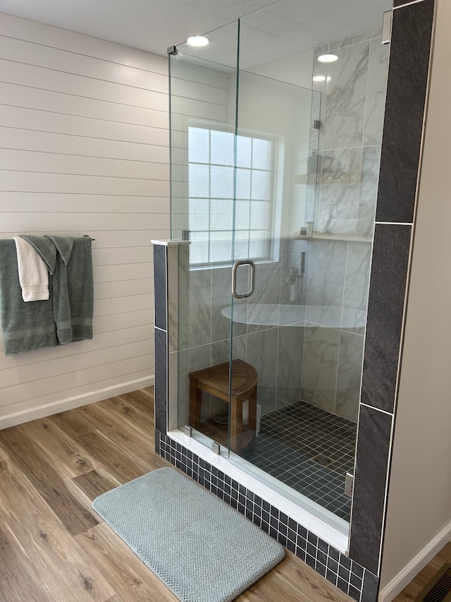 bathroom with a stall shower, wooden walls, baseboards, and wood finished floors