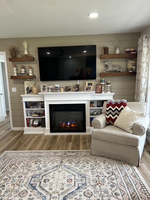 living area with a lit fireplace, wooden walls, and wood finished floors