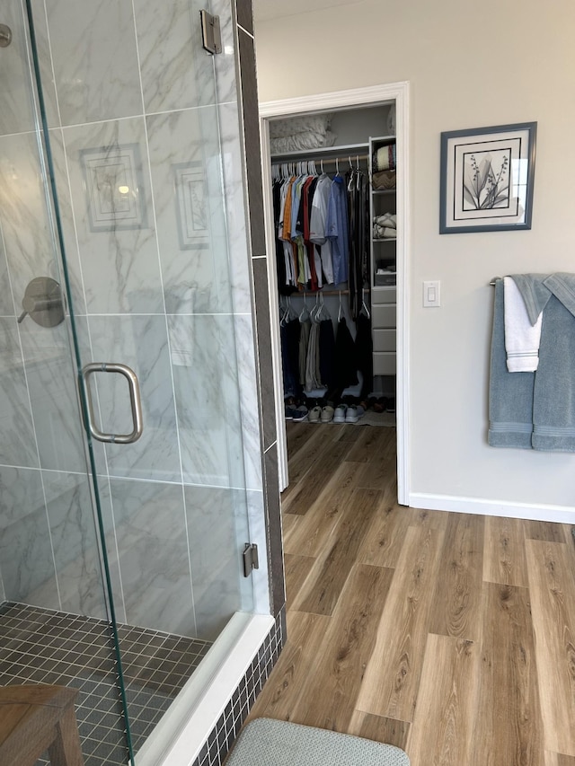 full bathroom with a shower stall, baseboards, a walk in closet, and wood finished floors