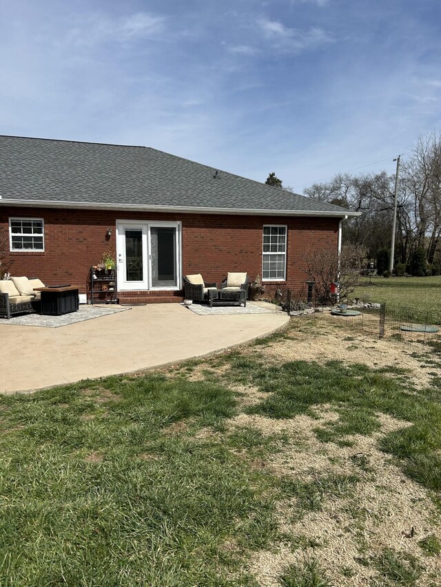 rear view of house featuring brick siding, roof with shingles, a lawn, and a patio