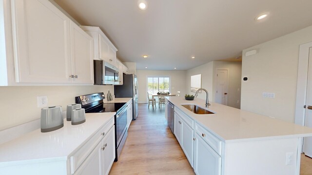 kitchen with a center island with sink, white cabinets, stainless steel appliances, light wood-type flooring, and a sink