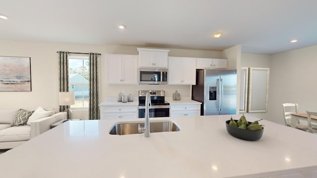 kitchen featuring a kitchen island with sink, white cabinetry, open floor plan, light countertops, and appliances with stainless steel finishes