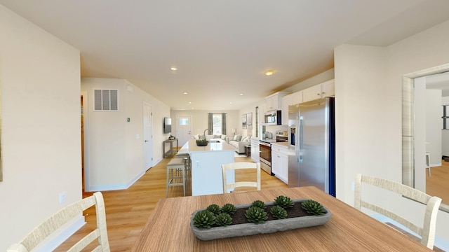 kitchen with light wood-style flooring, white cabinets, appliances with stainless steel finishes, an island with sink, and a kitchen bar