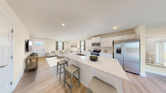 kitchen featuring a center island with sink, appliances with stainless steel finishes, white cabinets, a sink, and a kitchen bar