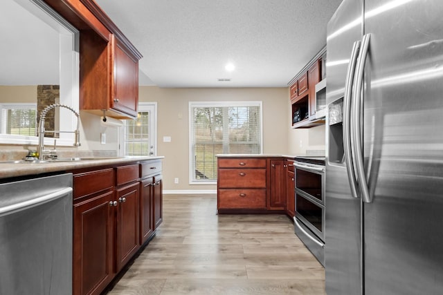 kitchen featuring stainless steel appliances, plenty of natural light, light wood-style floors, and a sink