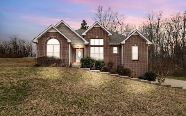 view of front of home with brick siding, a front yard, and a shingled roof