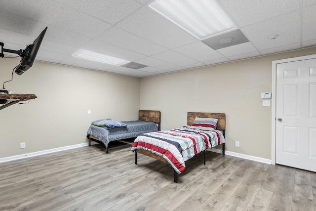 bedroom with a paneled ceiling, light wood finished floors, and baseboards