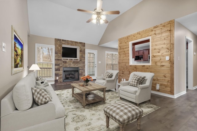 living area with ceiling fan, baseboards, wood finished floors, and a stone fireplace