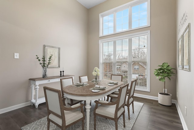 dining room with dark wood-style flooring, a high ceiling, and baseboards