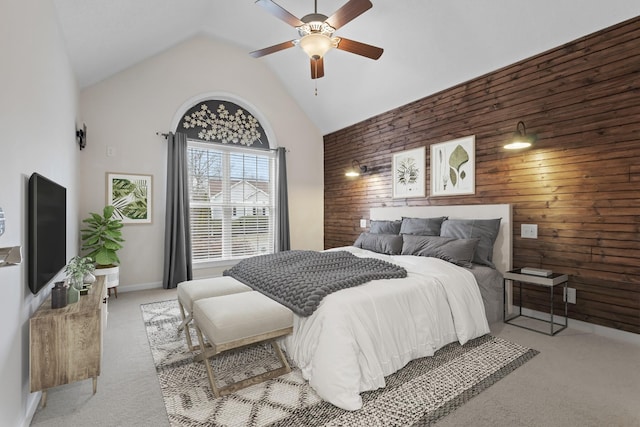 bedroom featuring ceiling fan, high vaulted ceiling, wooden walls, light colored carpet, and an accent wall