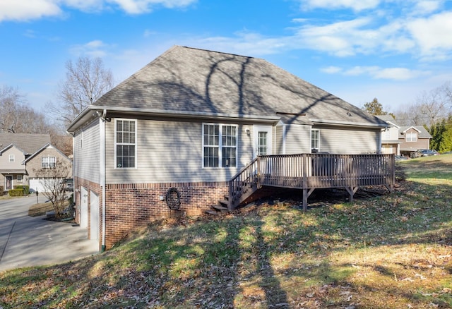 rear view of property with a garage, concrete driveway, roof with shingles, a wooden deck, and brick siding