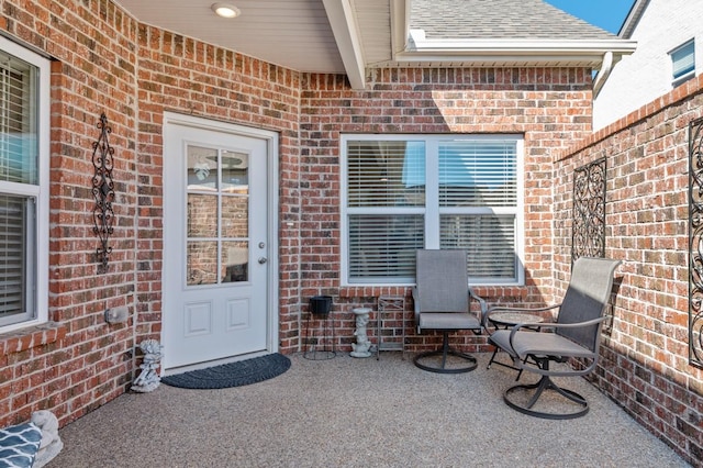 entrance to property with a patio area, roof with shingles, and brick siding