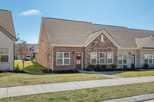 view of front of home featuring brick siding, a front yard, and a shingled roof