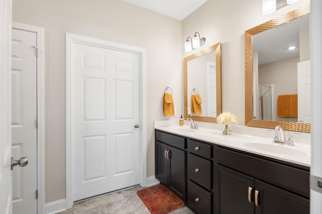 bathroom with double vanity, an enclosed shower, baseboards, and a sink