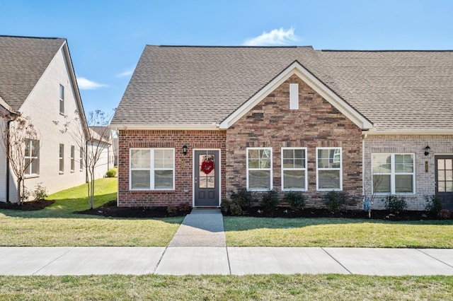 view of front of property with a front lawn, a shingled roof, and brick siding