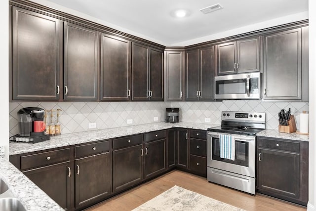 kitchen with dark brown cabinetry, visible vents, light wood-style flooring, appliances with stainless steel finishes, and light stone countertops