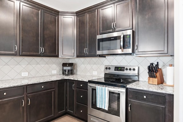 kitchen featuring stainless steel appliances, dark brown cabinets, decorative backsplash, and light stone counters