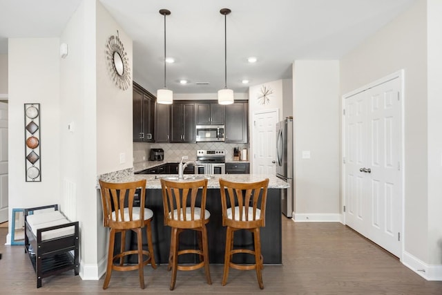 kitchen featuring light stone counters, dark brown cabinetry, stainless steel appliances, a peninsula, and tasteful backsplash